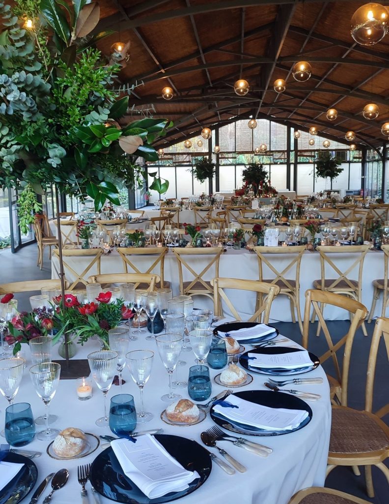 Salón de boda decorado con mesas elegantes, arreglos florales y ambiente cálido para la celebración.